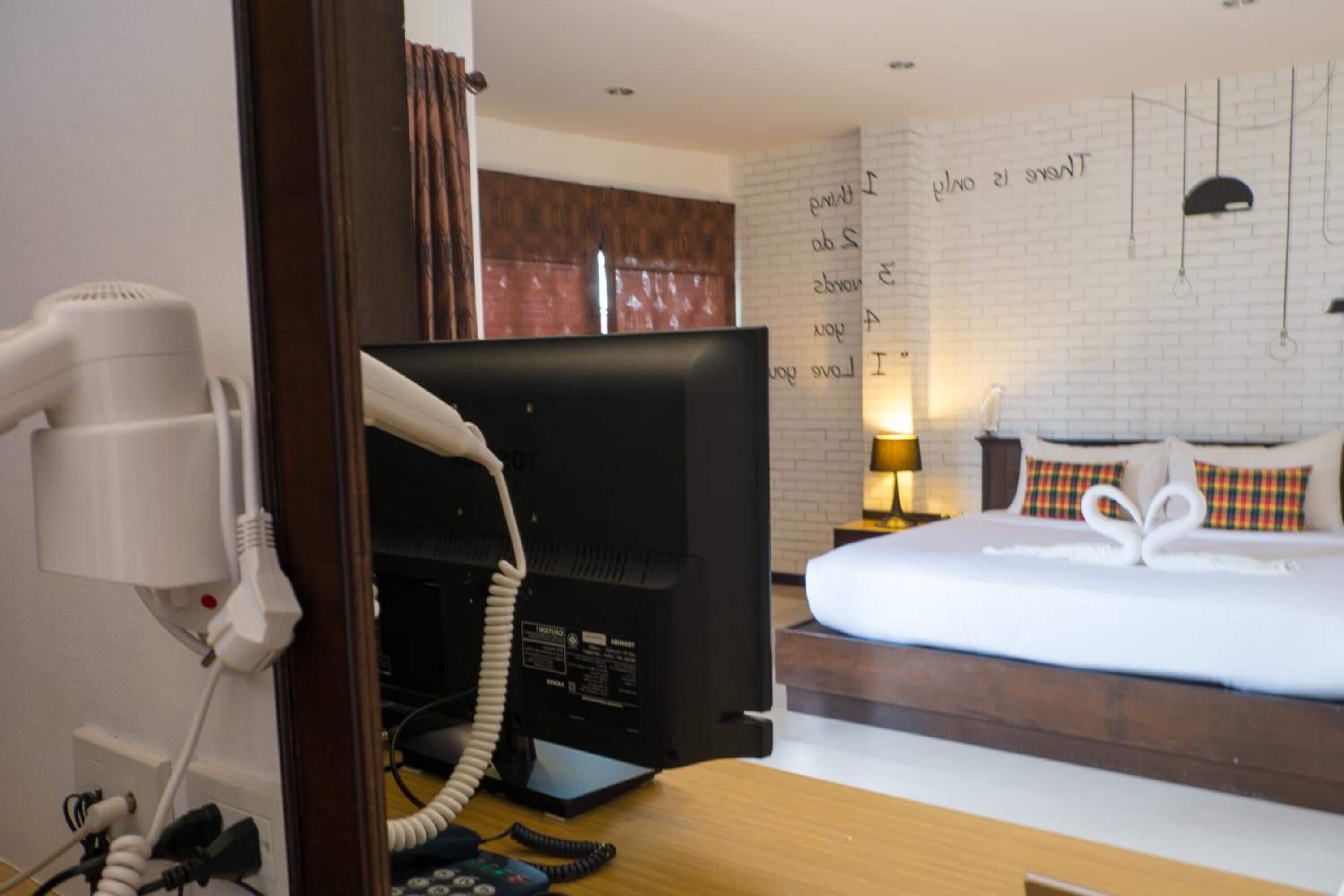 A hotel room with a bed, a desk with a computer, a hairdryer, and a wall with motivational quotes.