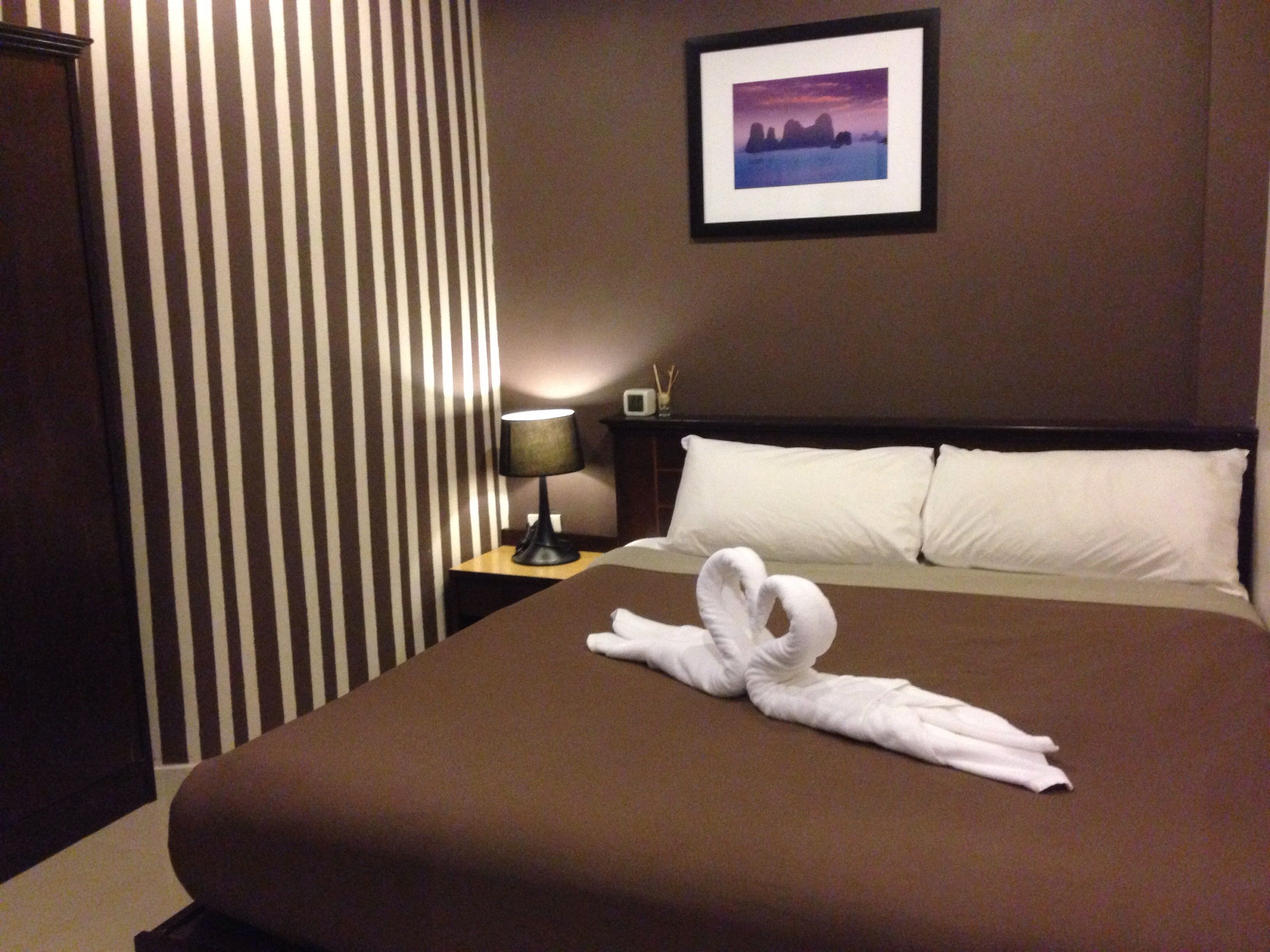 A hotel room with a neatly made bed, a framed picture on the wall, a lamp on a bedside table, and a striped curtain.