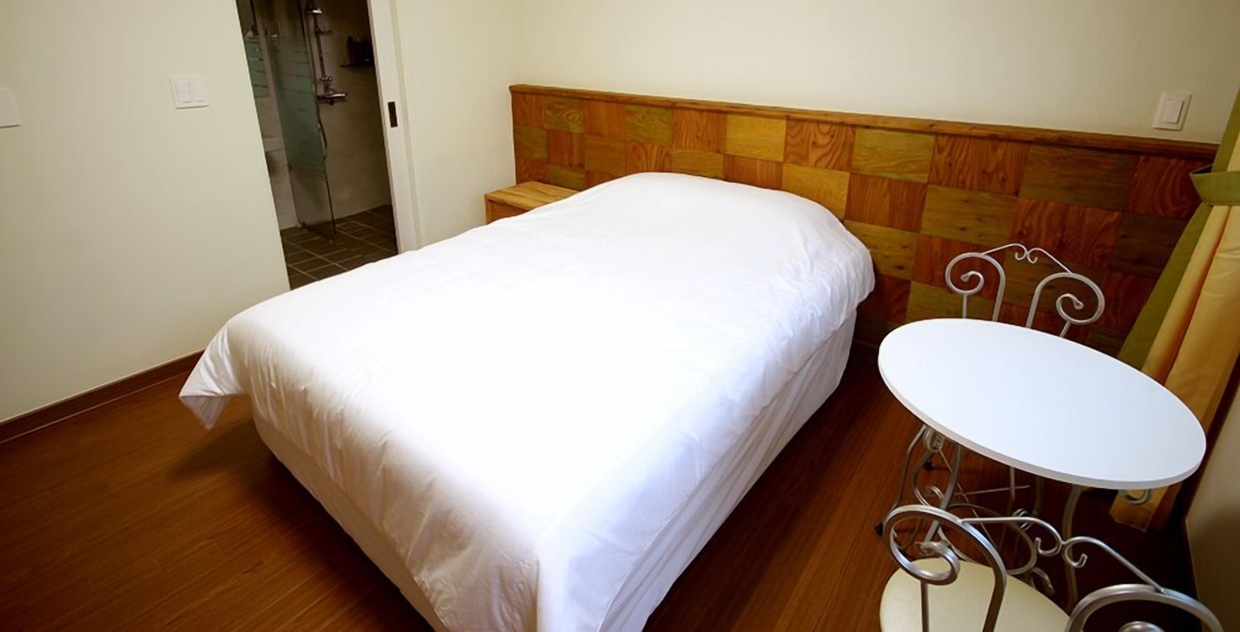 A single bed with a wooden headboard, a small bedside table, and a round table with a metal frame.