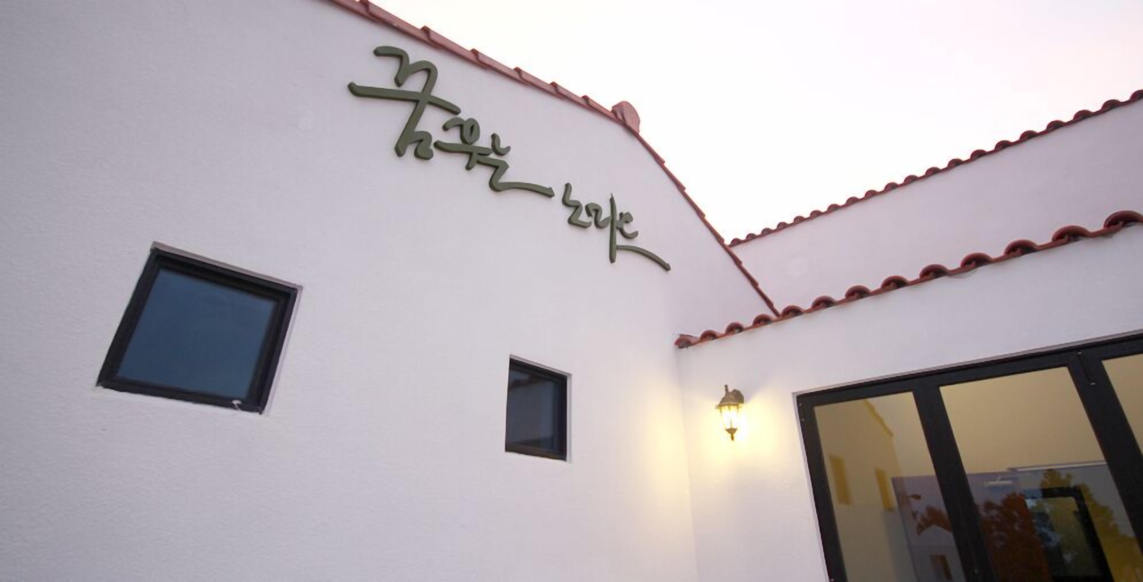 Un edificio con fachada blanca, una ventana pequeña y un letrero con letras verdes.