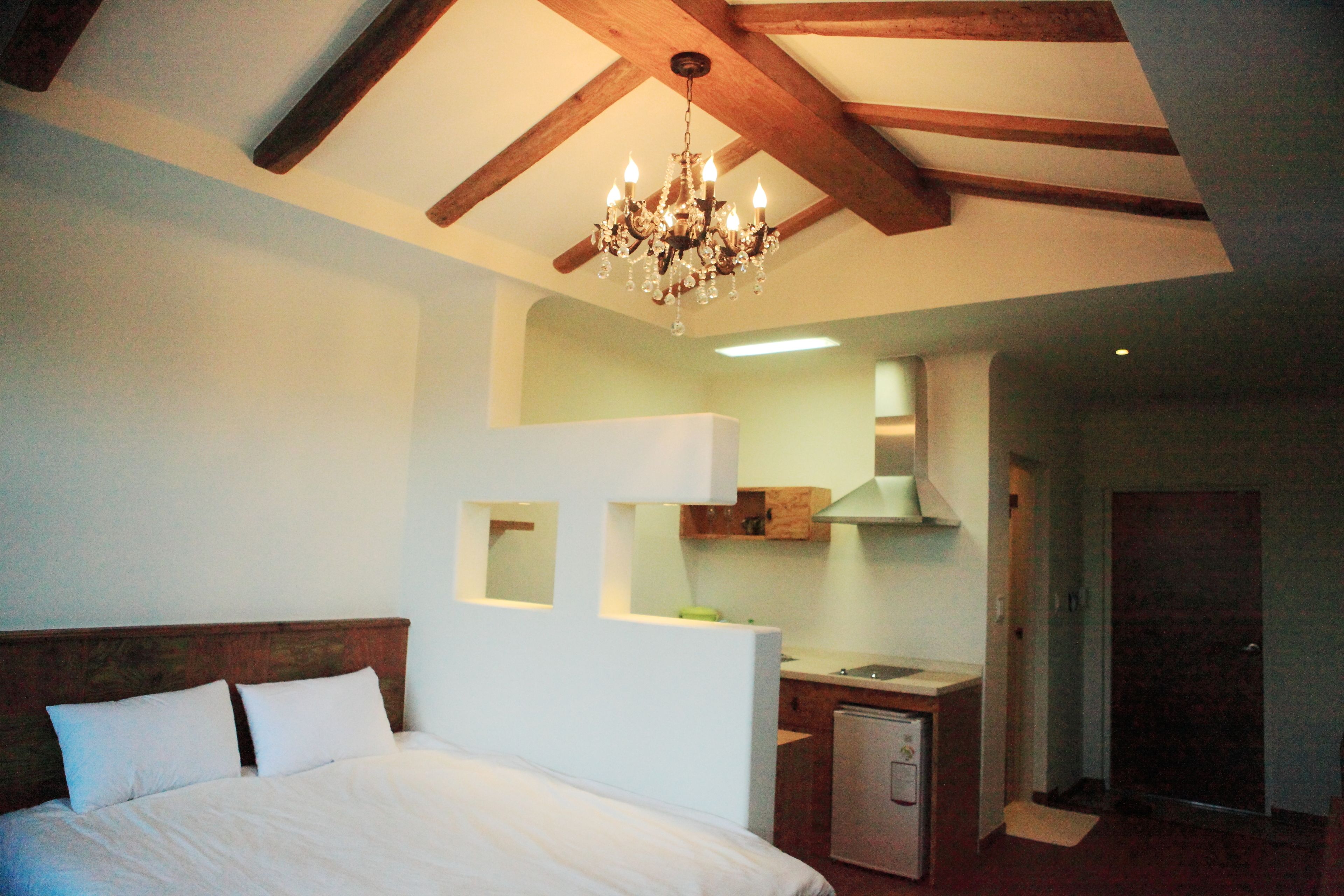 A bedroom with a large bed, a kitchenette, and a chandelier.