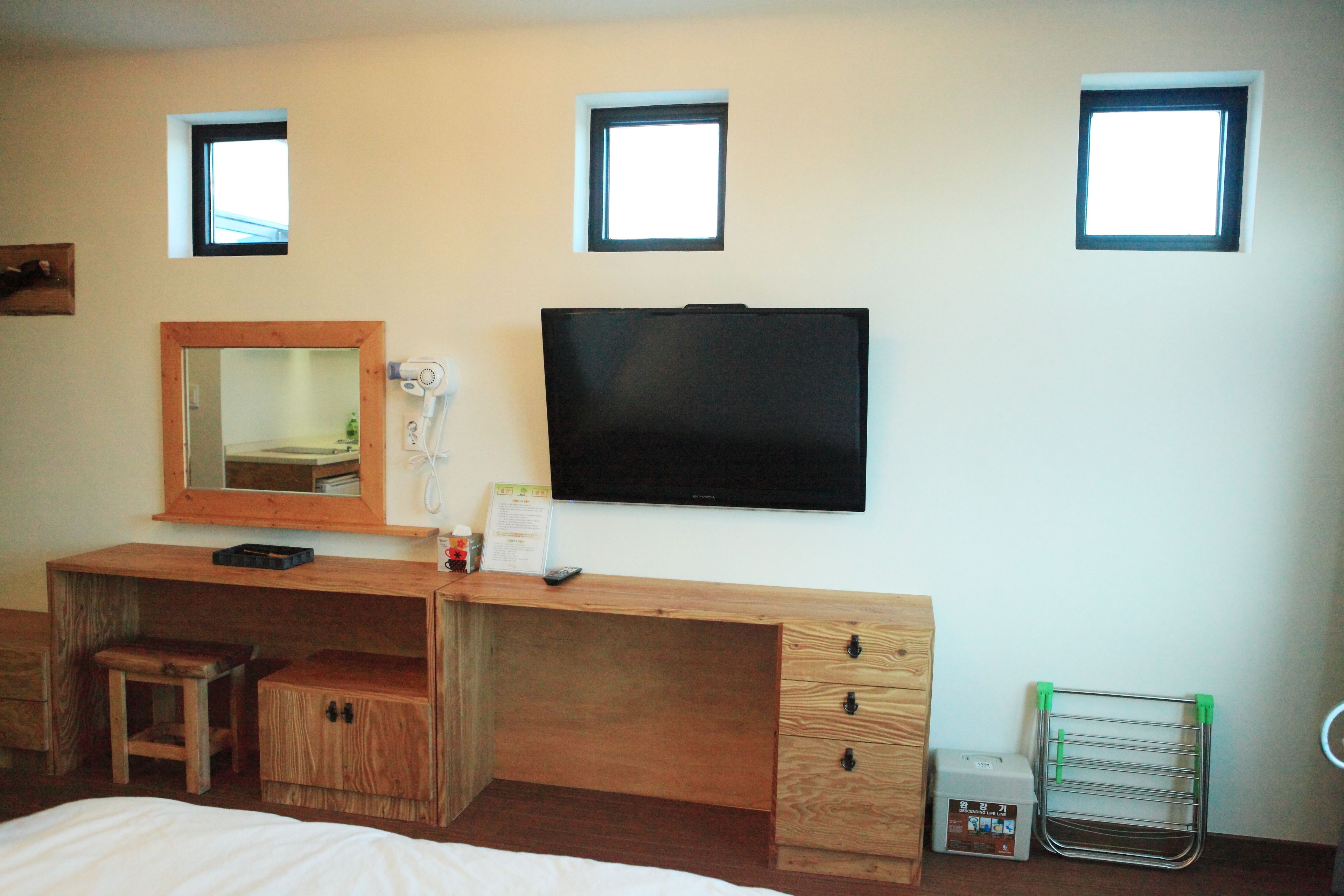 A hotel room with a wooden desk, a mirror, a television, and a small window.