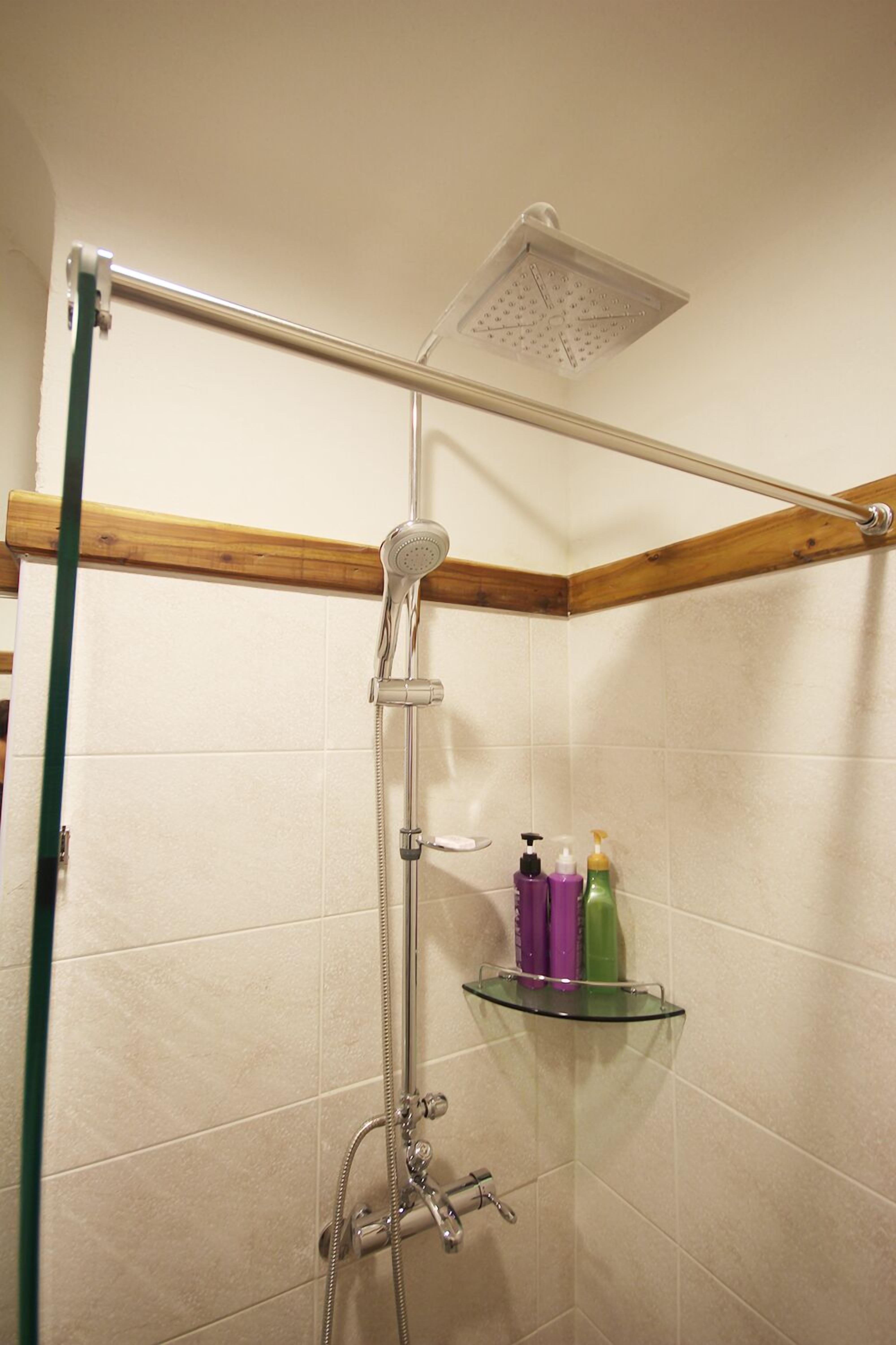 Ducha con cabezal de ducha de mano, estante de vidrio con artículos de aseo y techo con vigas de madera.