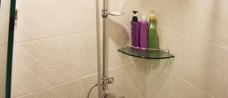 Ducha con cabezal de ducha de mano, estante de vidrio con artículos de aseo y techo con vigas de madera.