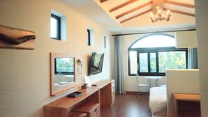 A bedroom with a wooden ceiling, a chandelier, a bed, a desk with a mirror, a television, and a window with curtains. - Nomad Pension in Jeju (Seogwipo)