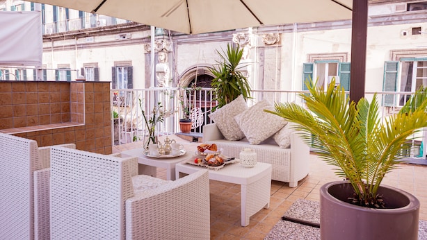 Una terraza con muebles de mimbre blanco, una planta en maceta y una mesa con comida y bebidas.