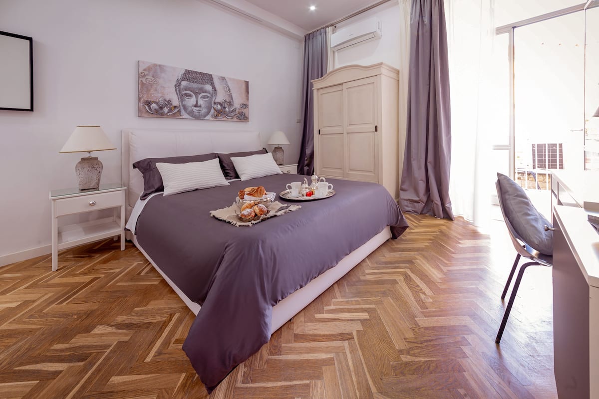 A bedroom with a bed, a nightstand, a lamp, a wardrobe, a chair, and a window.