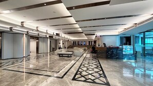 A spacious lobby with a central seating area, a reception desk, and a large glass window. - Grace Hotel (Bangkok)