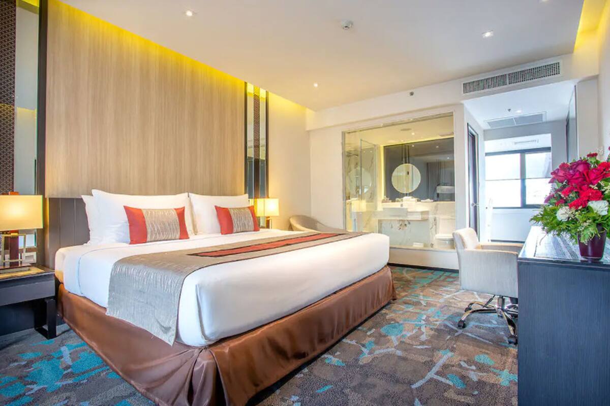 A modern hotel room with a large bed, a desk, and a bathroom visible through an open door.