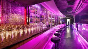 A bar with a long counter and stools, a patterned wall, and a modern interior design. - Grace Hotel (Bangkok)