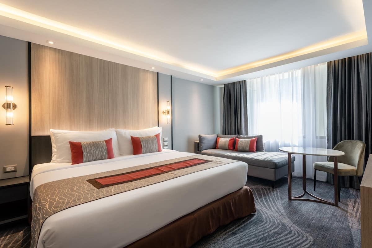 A modern hotel room with a large bed, a sofa, a small table, and a chair.