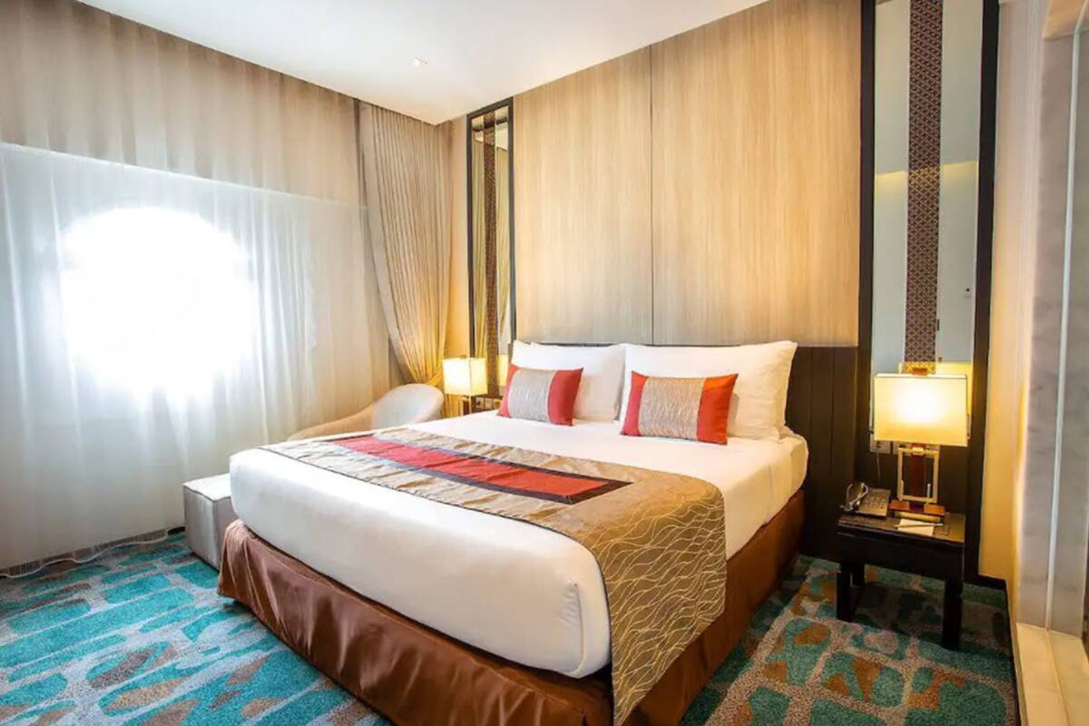 A hotel room with a large bed, two bedside tables with lamps, a chair, and a window with curtains.