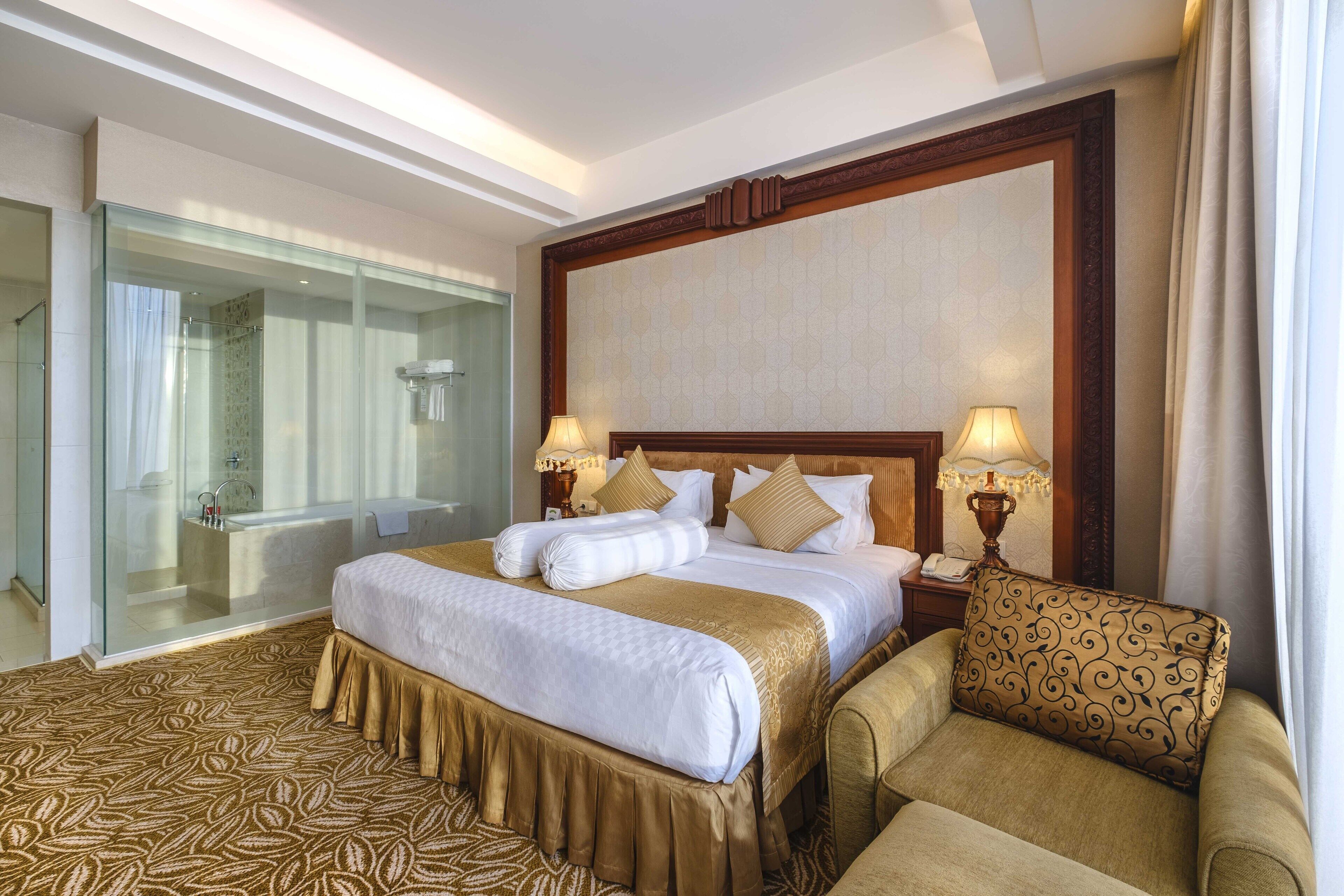 A hotel room with a large bed, a glass-enclosed shower, a sofa, and two bedside lamps.