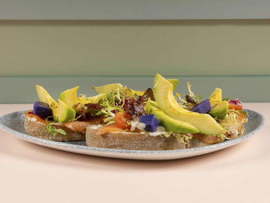 A plate with three slices of toast topped with avocado, tomato, and greens.