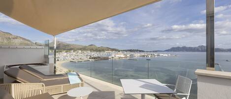 A terrace with lounge chairs, a table, and a view of a marina and beach.