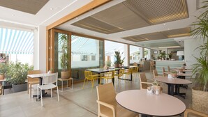 Un área de comedor moderna con varias mesas y sillas, ventanas amplias y plantas de interior.