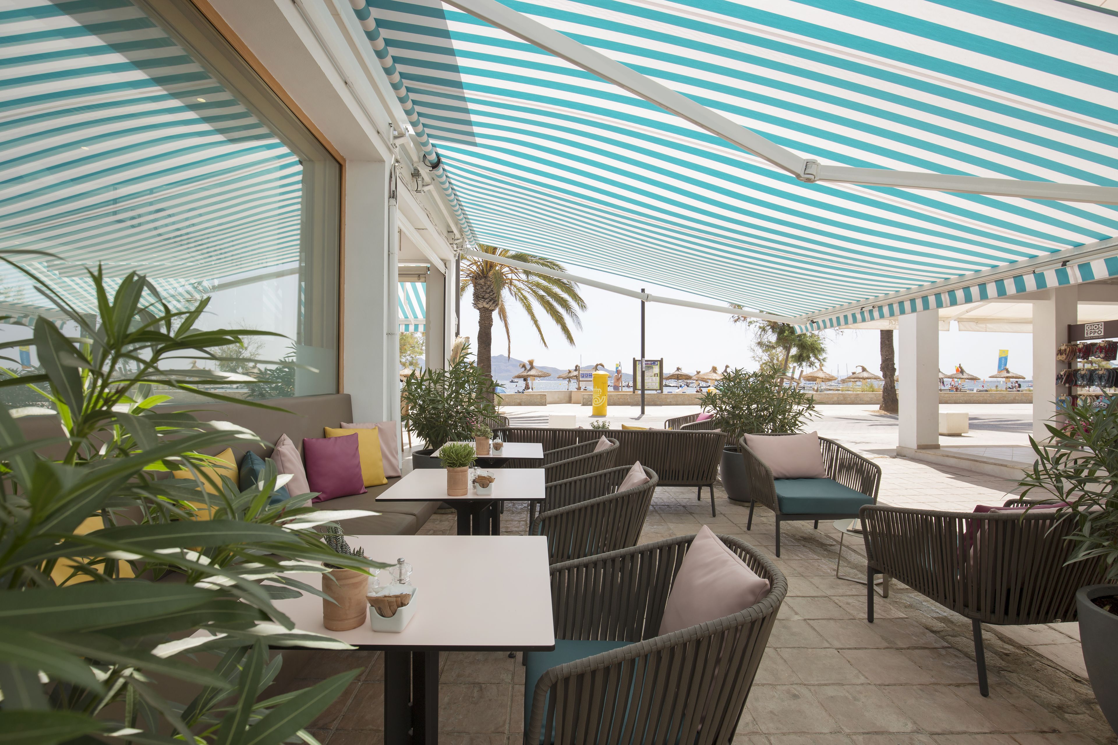 An outdoor patio area with striped awnings, wicker furniture, and potted plants.
