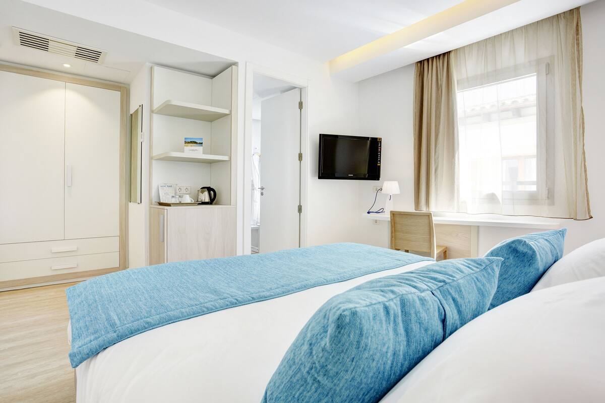 A hotel room with a bed, a TV, a desk, and a wardrobe.