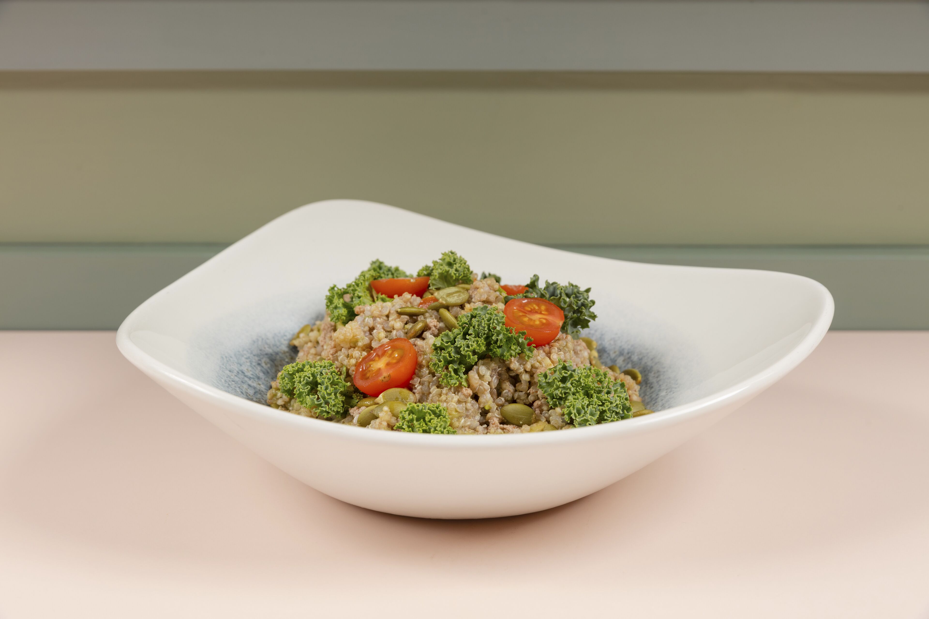 Un tazón blanco de forma original con ensalada, tomates y hojas verdes.