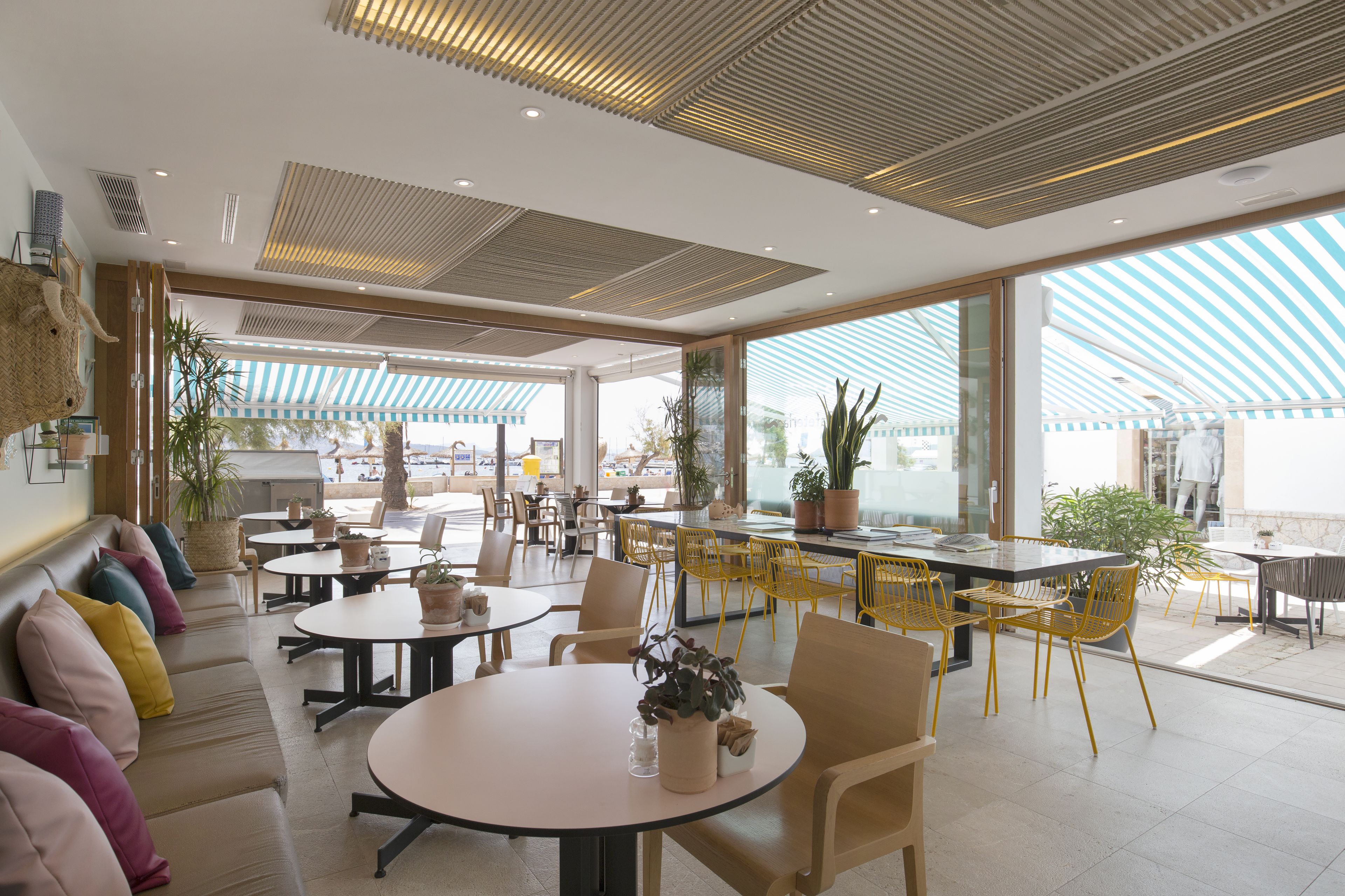 A modern cafe with round tables, yellow chairs, and a large window offering a view of the street.