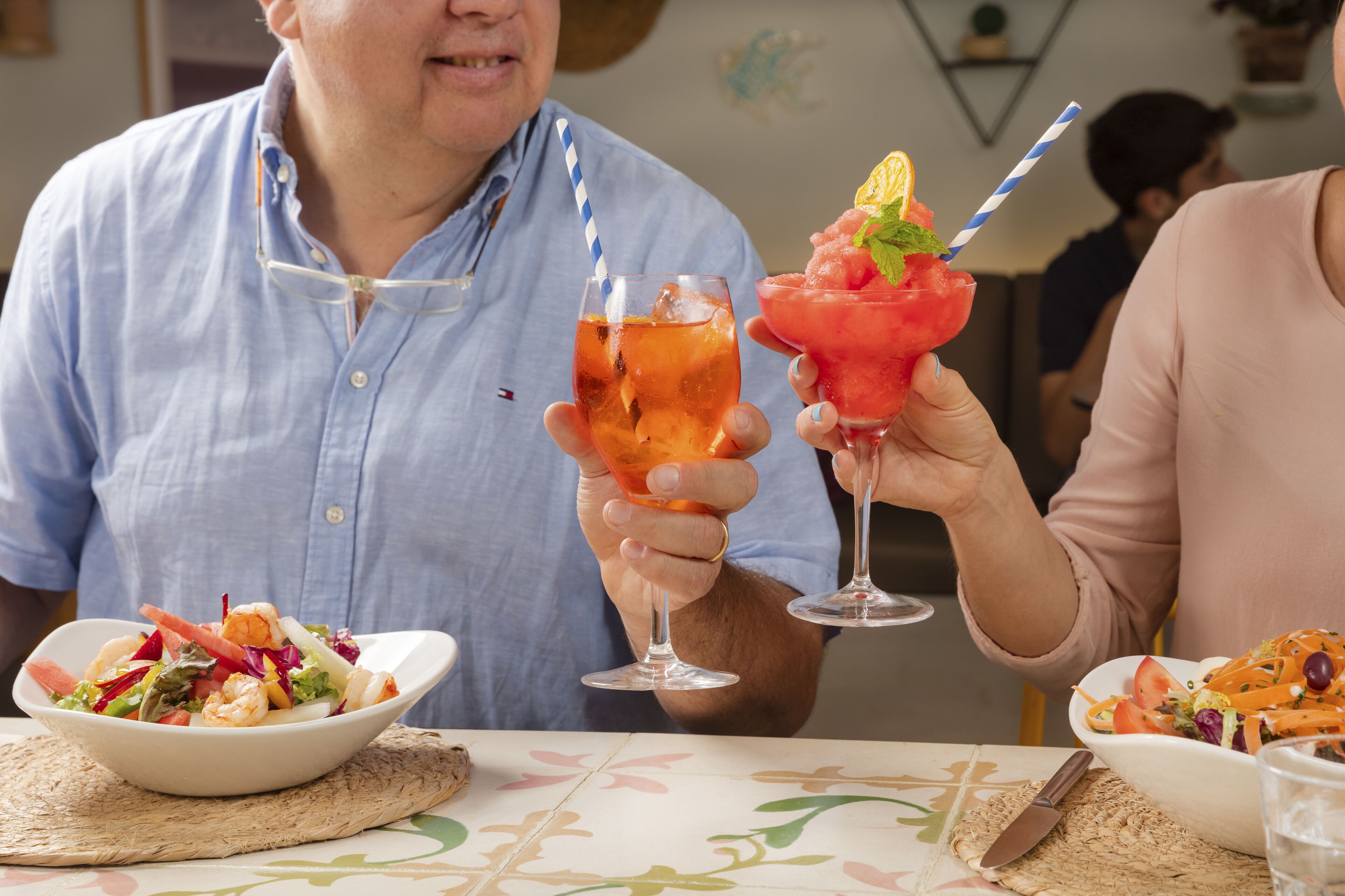Een eettafel met een salade, een cocktail en een vruchtensap.