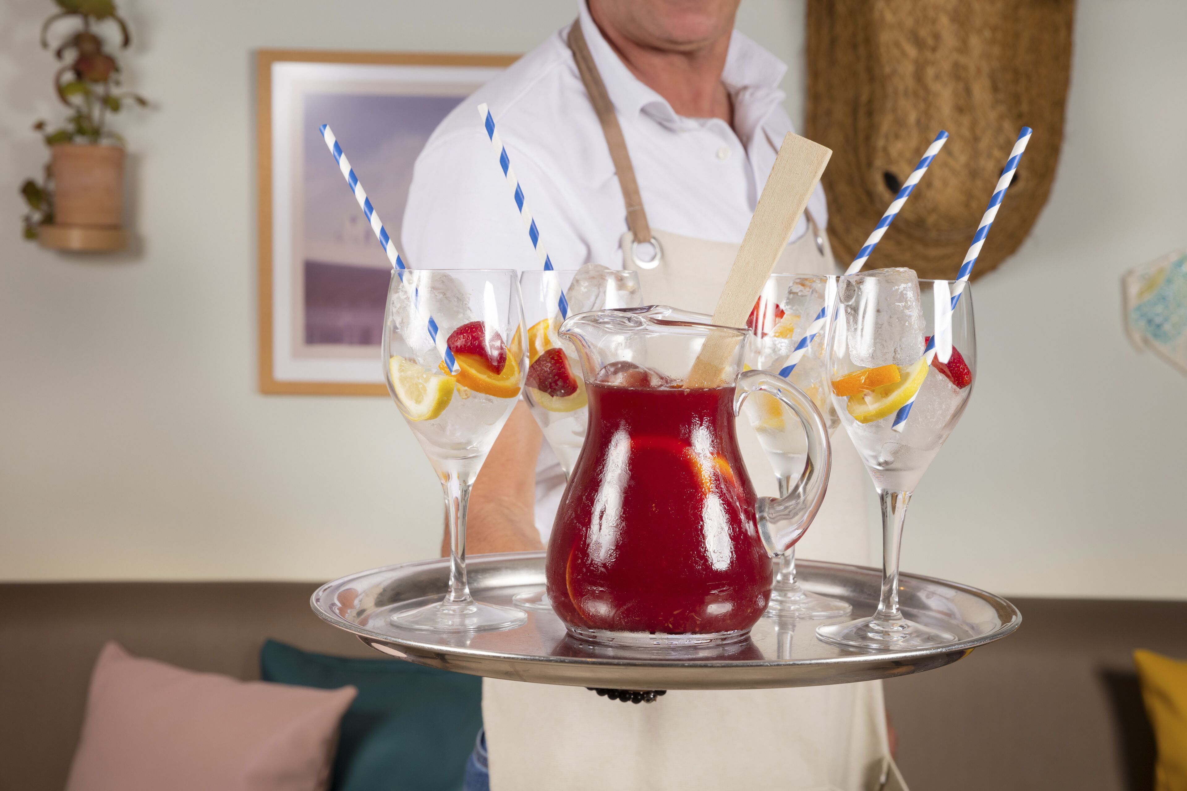 Una bandeja con una jarrón y dos vasos de bebida roja, decorada con fruta, sobre una bandeja de metal.
