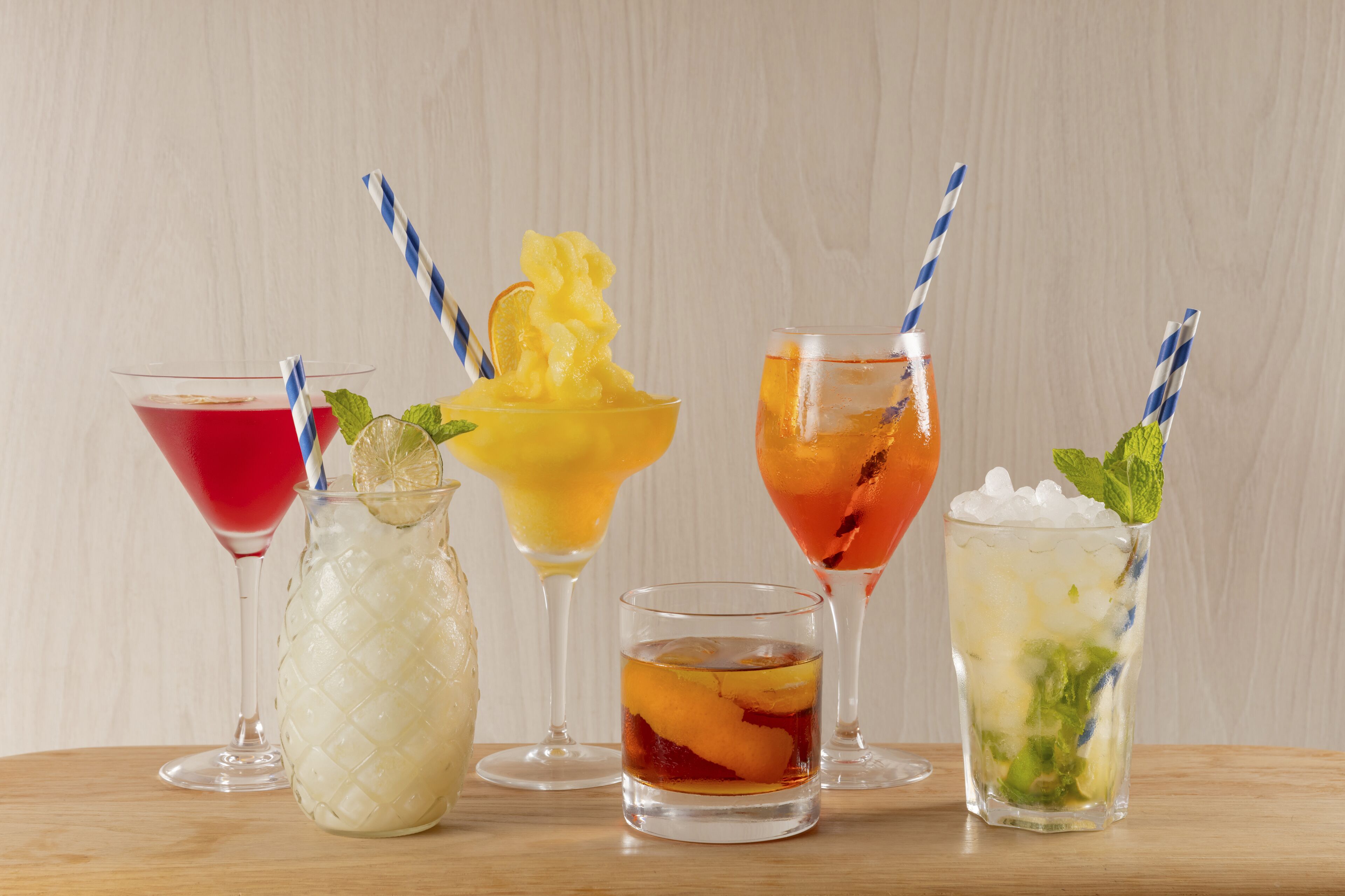 Variedad de bebidas en distintos vasos, incluyendo un cóctel rojo, un trago dulce amarillo, un cóctel naranja y un cóctel verde con menta.