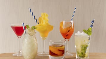 Variedad de bebidas en distintos vasos, incluyendo un cóctel rojo, un trago dulce amarillo, un cóctel naranja y un cóctel verde con menta.