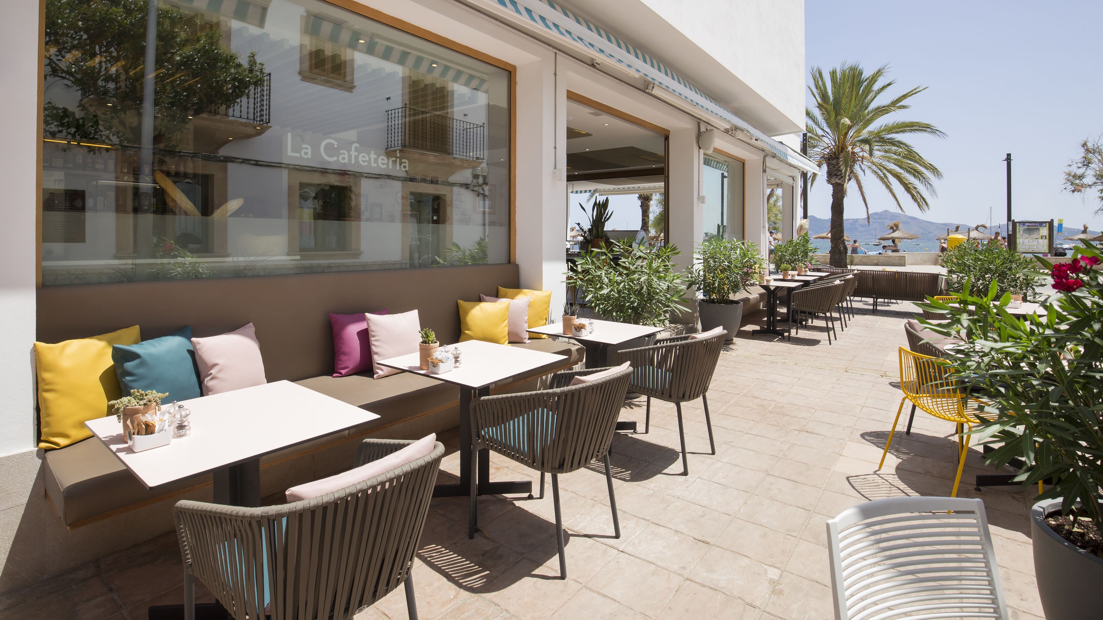 Un área de café al aire libre con mesas, sillas, plantas en macetas y vistas al mar.