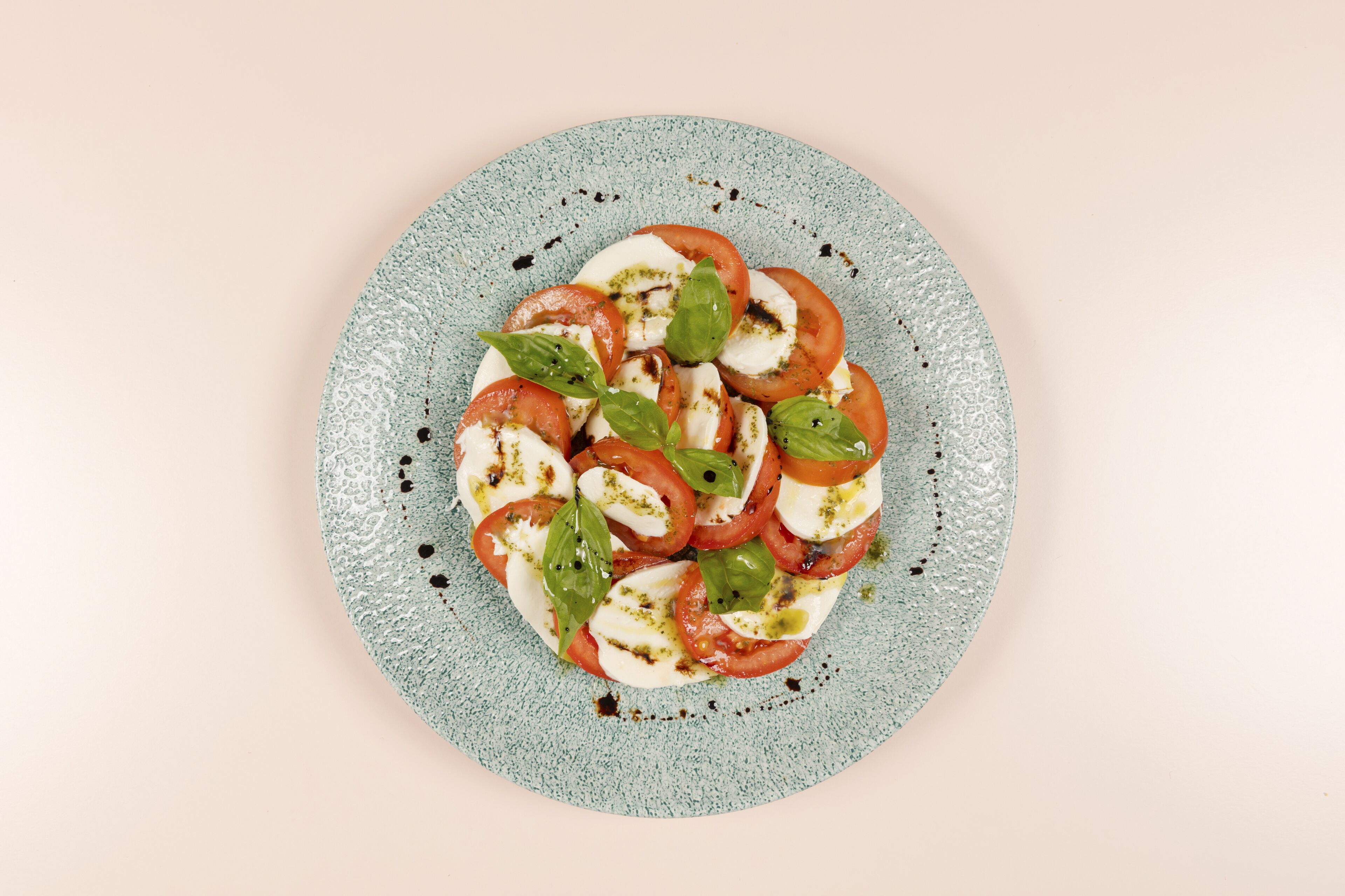 Un plato de ensalada caprese con tomates, mozzarella y albahaca sobre un plato moteado.