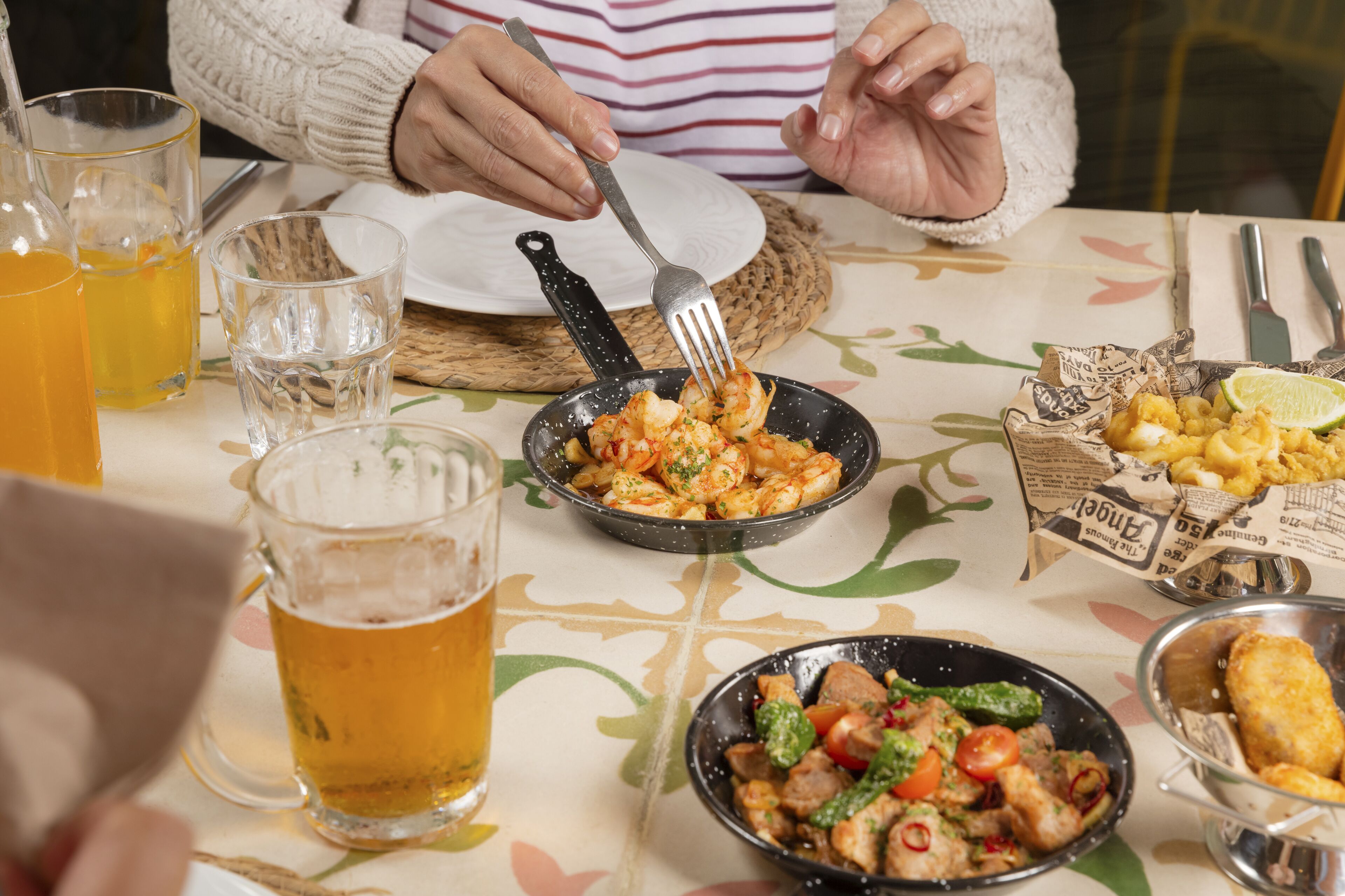 Una mesa de comedor con varios platos, vasos de cerveza y cubiertos.