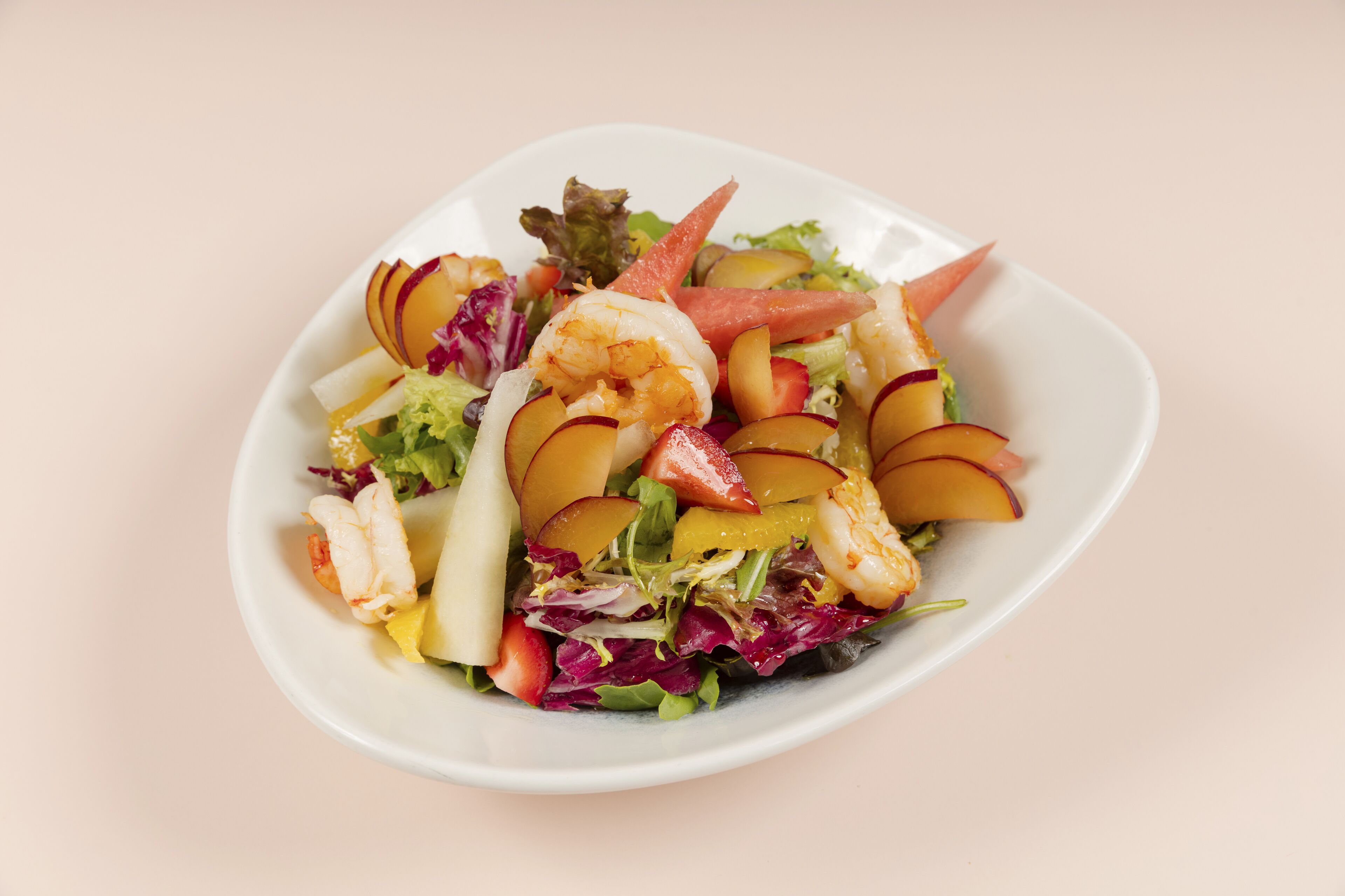 Un plato blanco con una ensalada de camarones, rodajas de manzana y hojas verdes mezcladas.