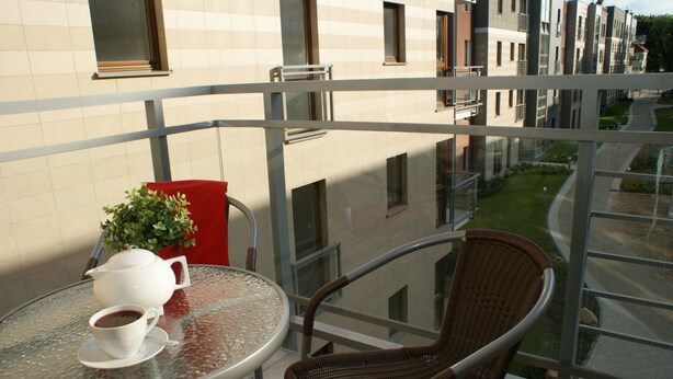 Un balcon avec une table en verre, une chaise en osier, une chaise rouge, une théière blanche et une tasse de café.