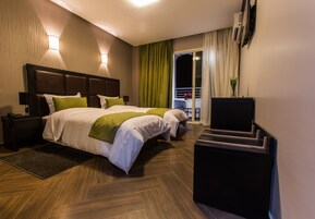Habitación de hotel con dos camas, un escritorio, un televisor y un balcón con cortinas.