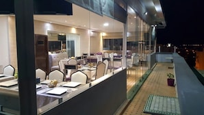 En restaurang med en modern inredning, med glasväggar, vita och lila stolar och ett kaklat golv.