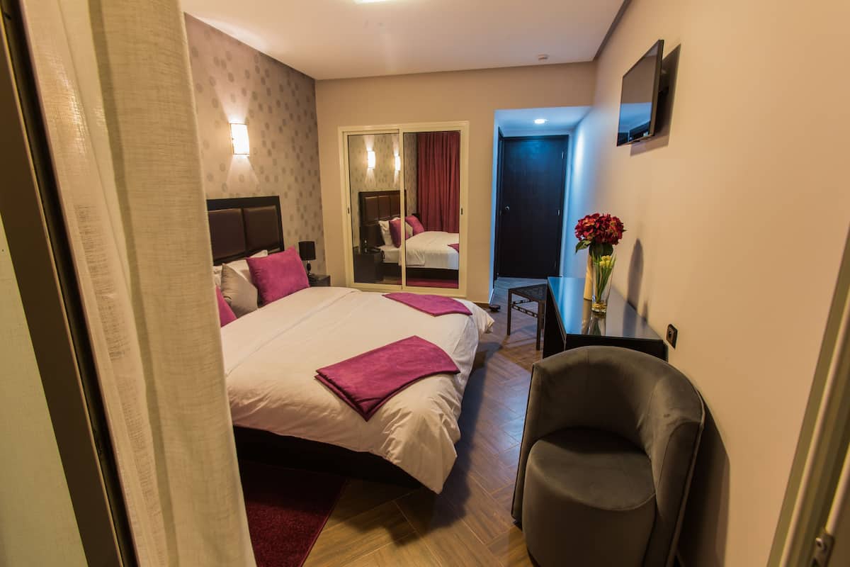A hotel room with a large bed, a chair, a desk, and a mirror.