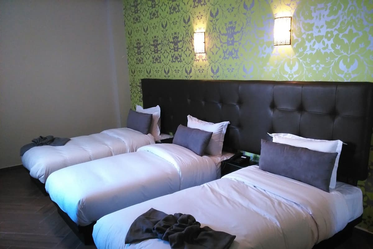 A hotel room with three single beds, a dark headboard, and patterned wallpaper.