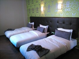 Una habitación de hotel con tres camas individuales, un cabecero oscuro y papel tapiz estampado.
