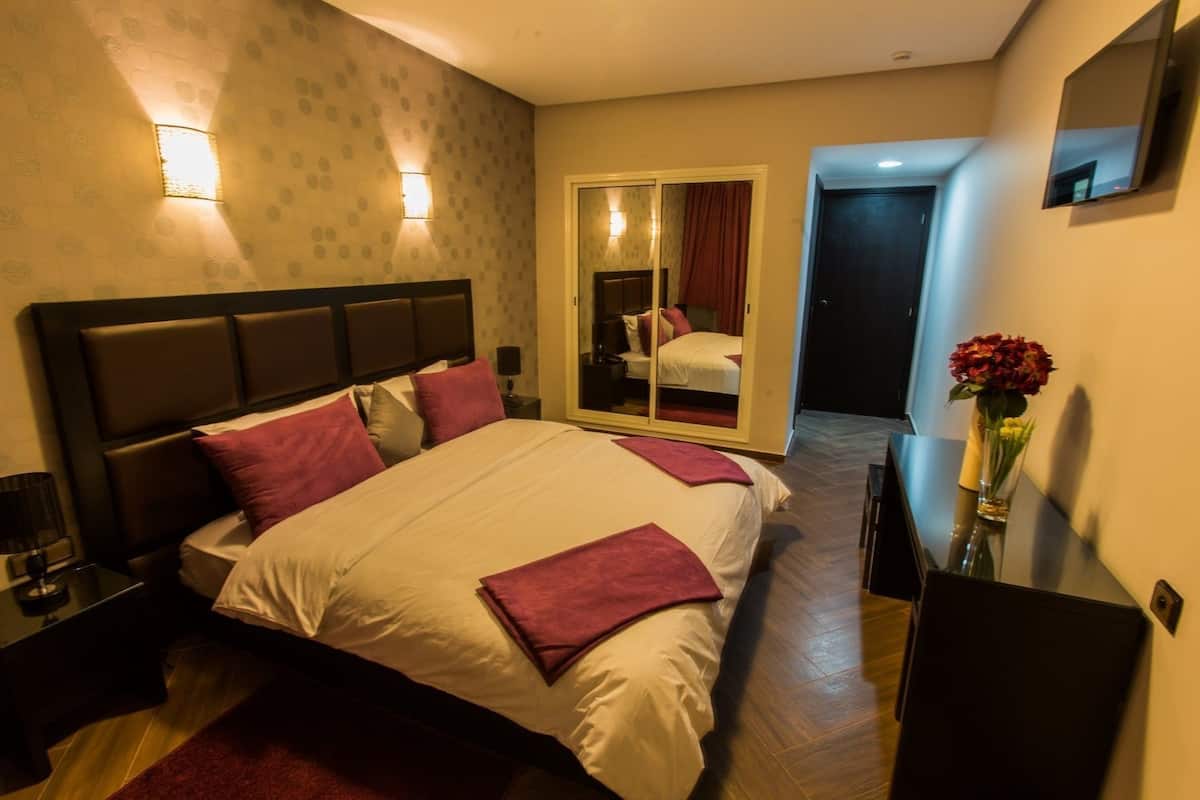 A hotel room with a bed, a nightstand, a desk, a mirror, and a sliding door leading to a bathroom.