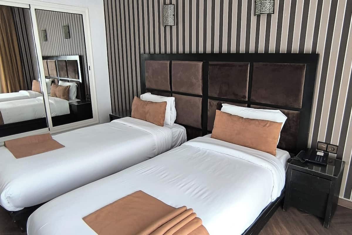 A hotel room with two single beds, a large mirror, a bedside table with a phone, and a striped wall design.