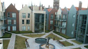 Un patio con una fuente central, bancos y una estatua. Edificios circundantes presentan diversos estilos arquitectónicos.