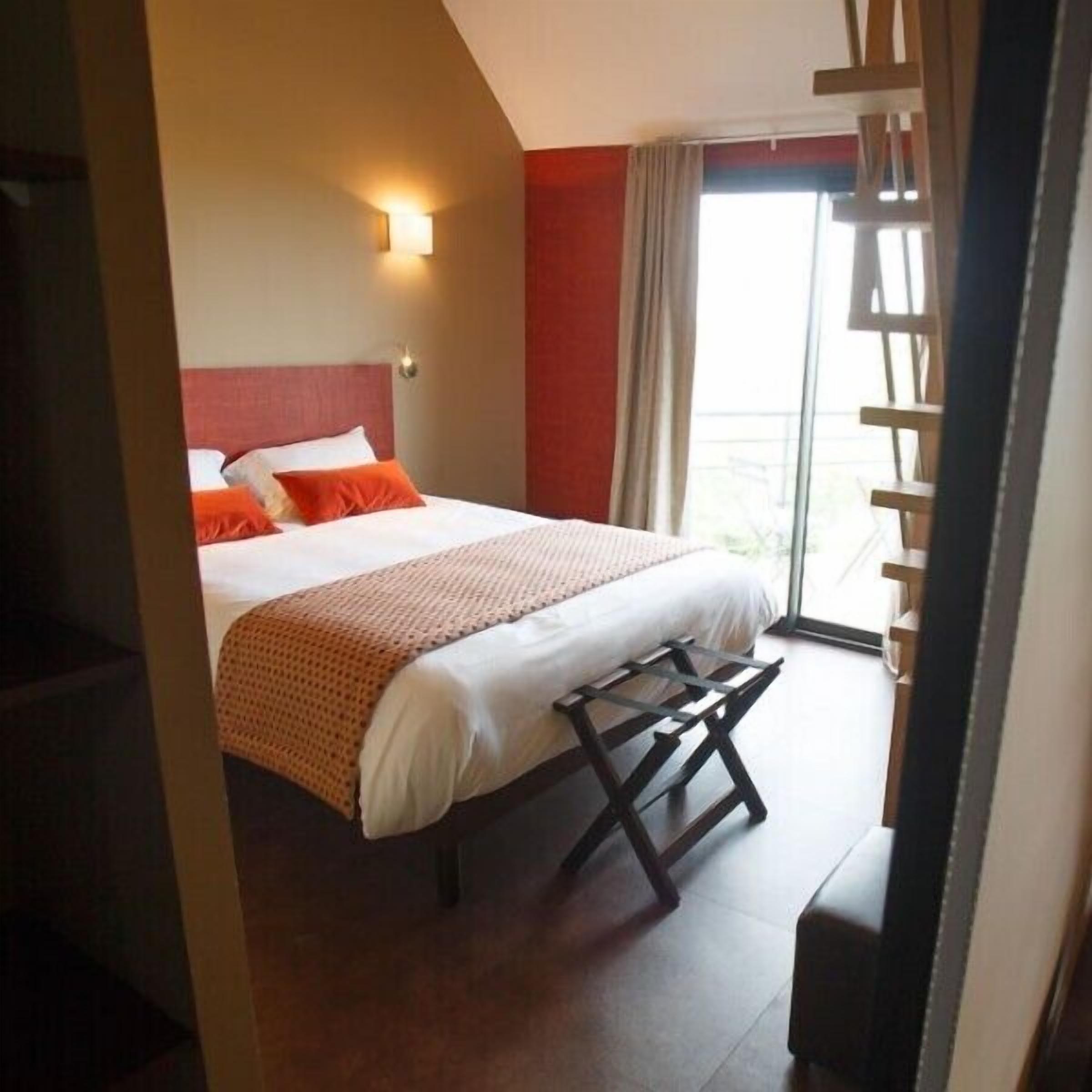 A hotel room with a bed, a nightstand, a window with curtains, and a balcony.