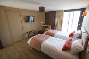 A hotel room with two beds, a TV, a chair, and a window with curtains.