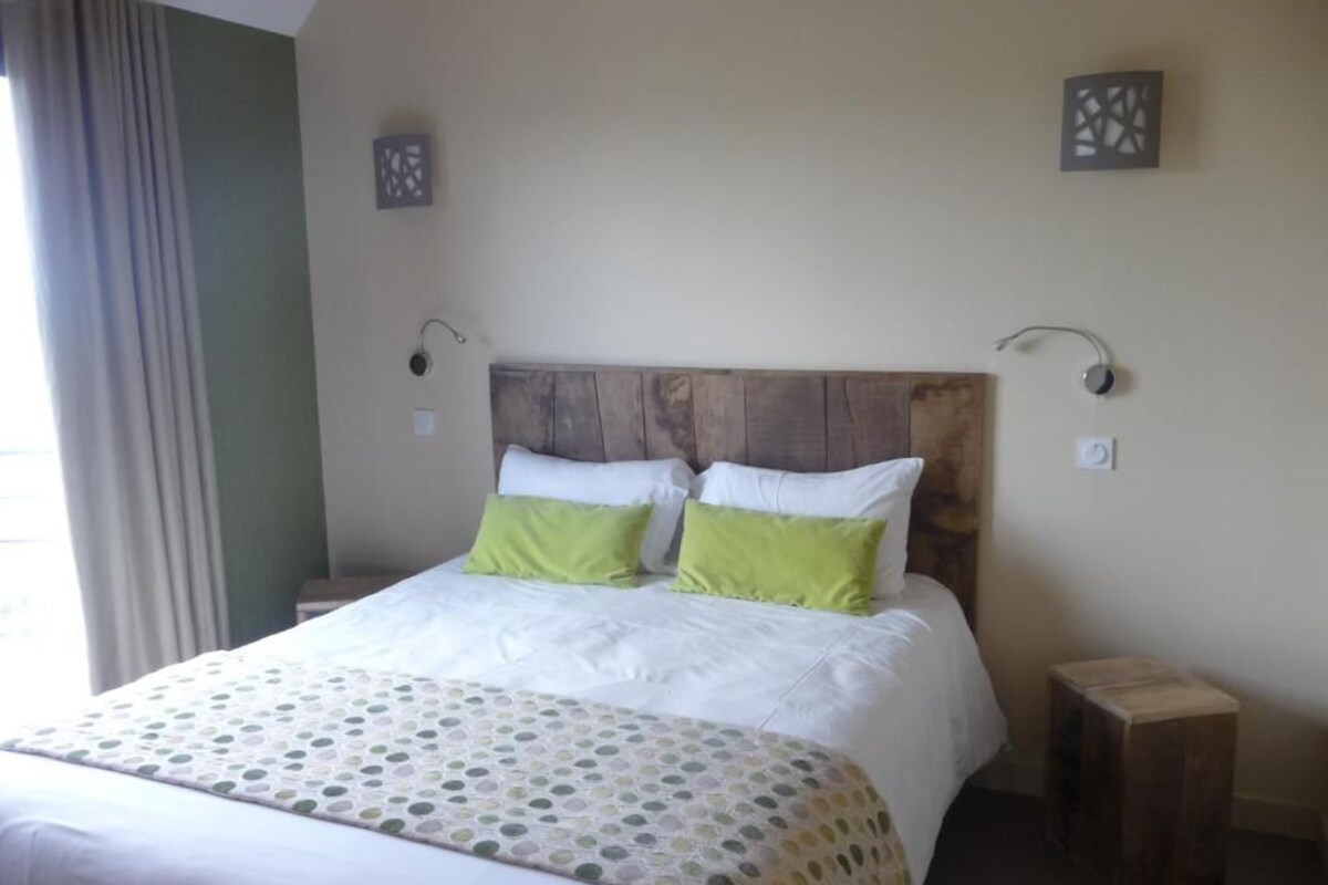 Un lit bien fait, avec une tête de lit en bois, deux tables de chevet et une fenêtre avec des rideaux.