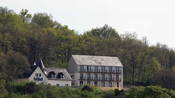 Een hotel met een witte gevel, meerdere balkons en een steil dak, omgeven door dicht bos.