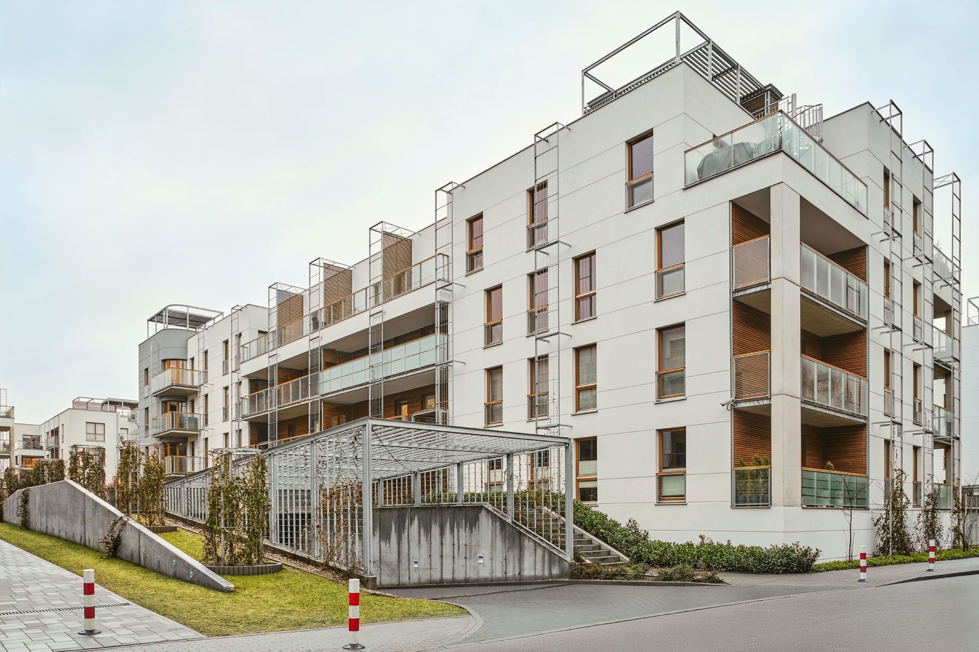 A modern multi-story residential building with balconies, a covered outdoor seating area, and a staircase leading to the entrance.