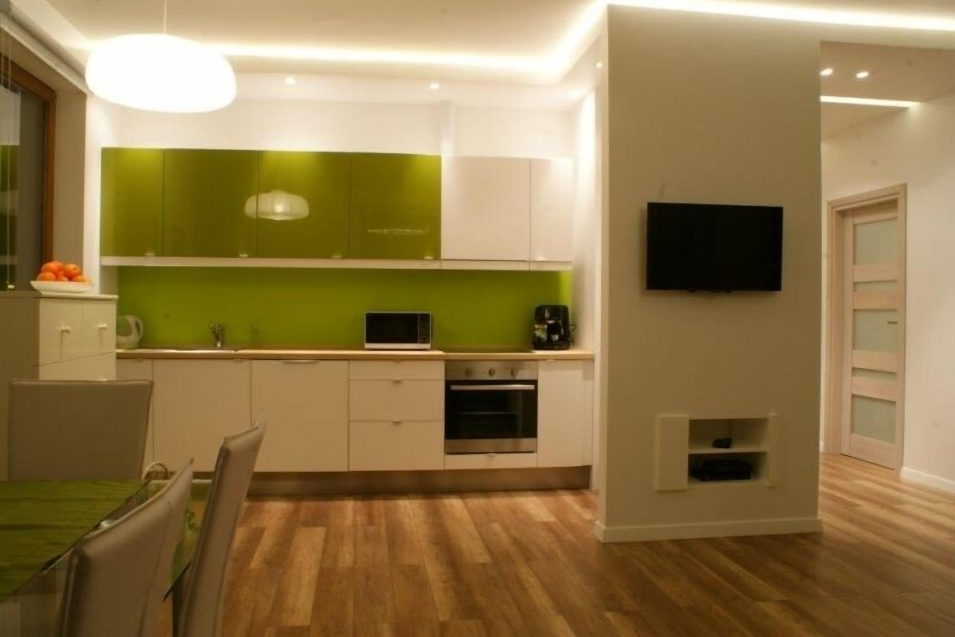 Una cocina moderna con armarios verdes, horno empotrado y televisor montado en la pared.