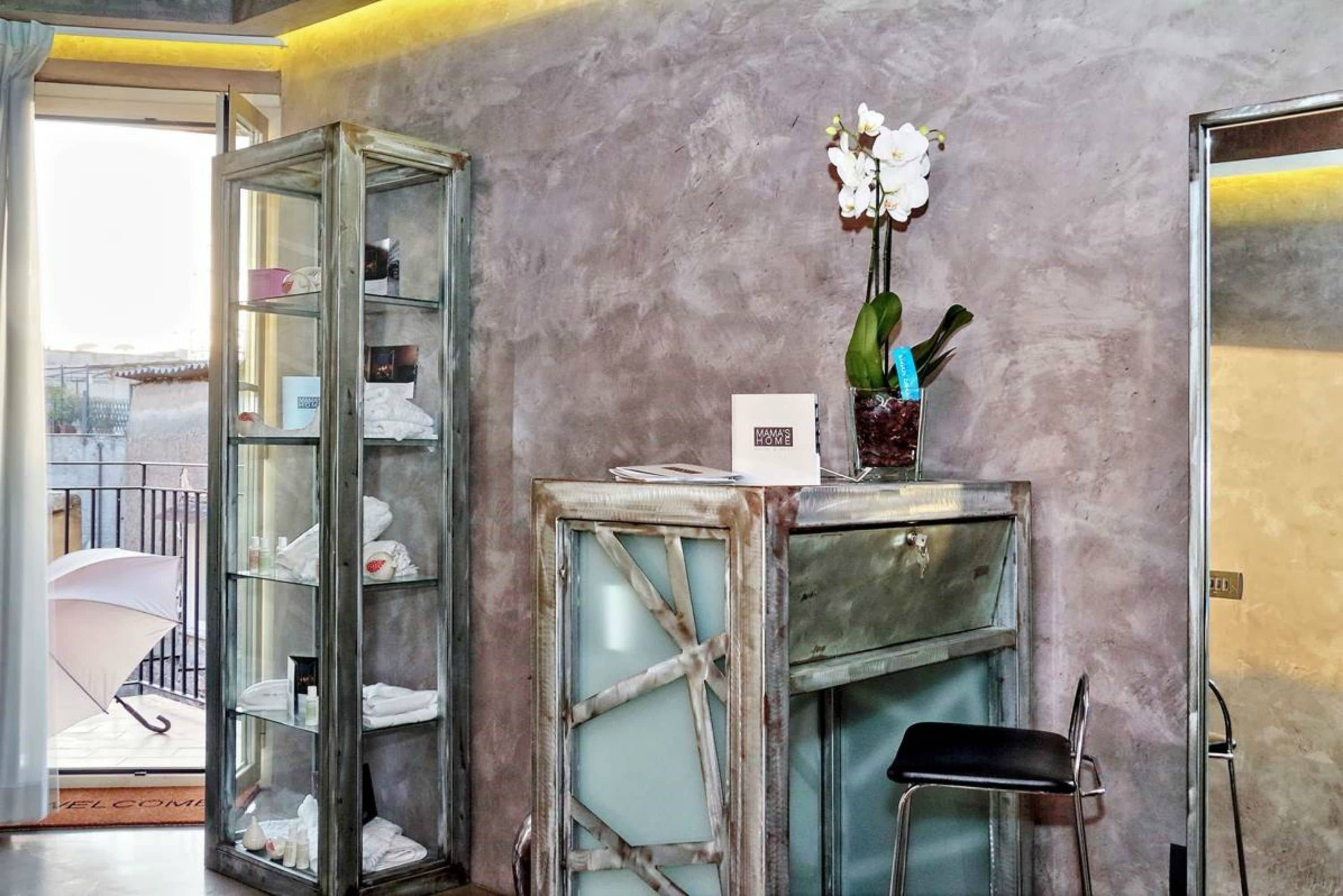 A hotel reception area with a glass display case containing toiletries, a small table with a vase of white orchids, and a chair.