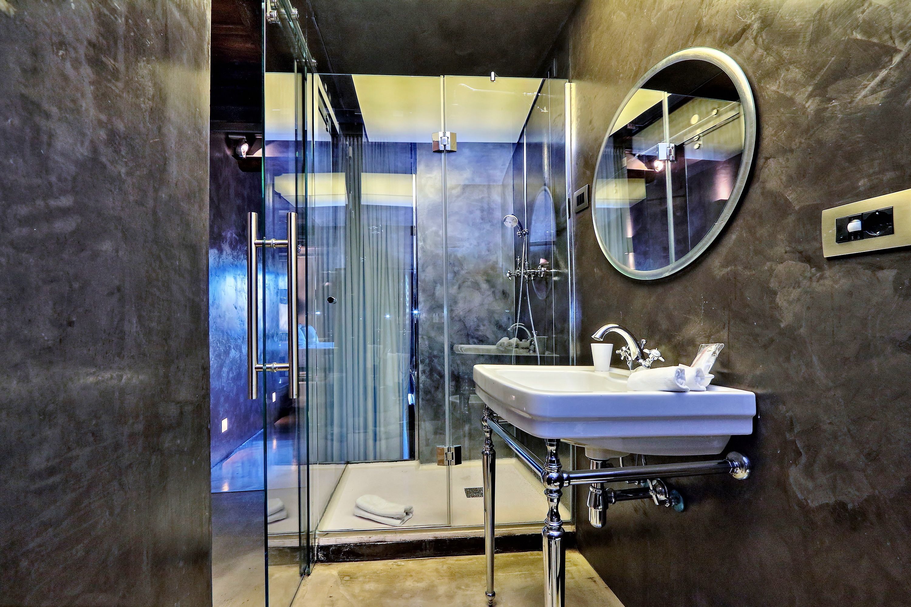 A modern bathroom with a glass-enclosed shower, a white sink, and a round mirror.