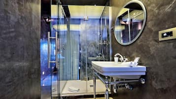 A modern bathroom with a glass-enclosed shower, a white sink, and a round mirror.